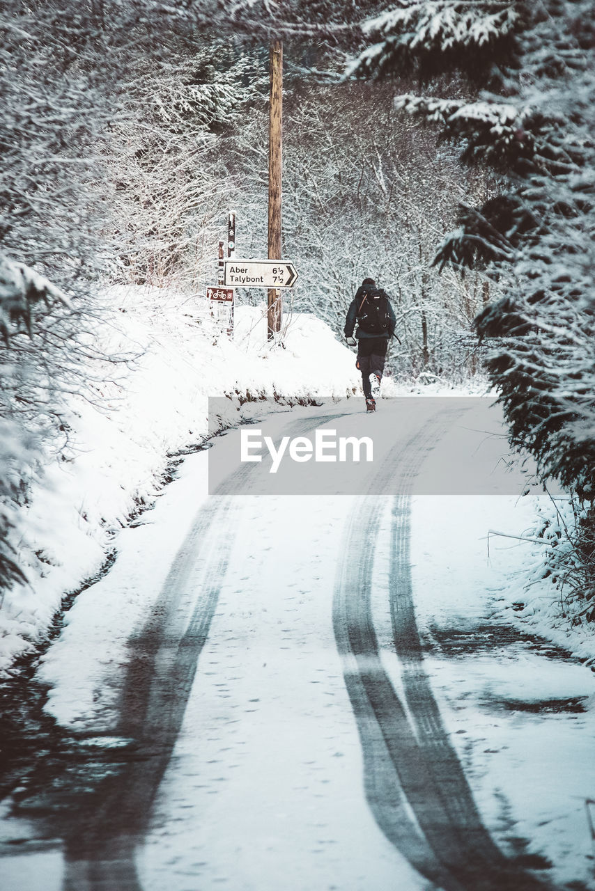 REAR VIEW OF PERSON WALKING ON SNOW COVERED STREET