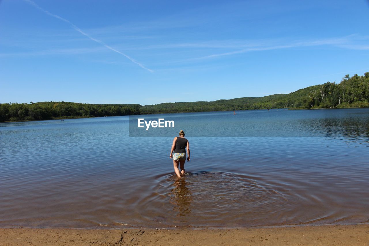 Rear view of woman walking in lake against blue sky