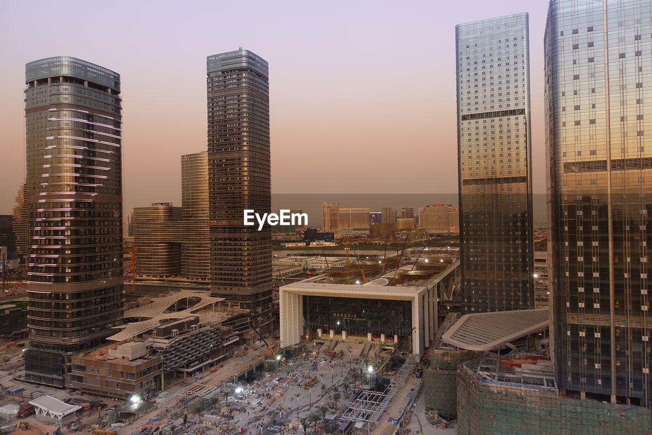 HIGH ANGLE VIEW OF MODERN BUILDINGS IN CITY AGAINST SKY DURING SUNSET