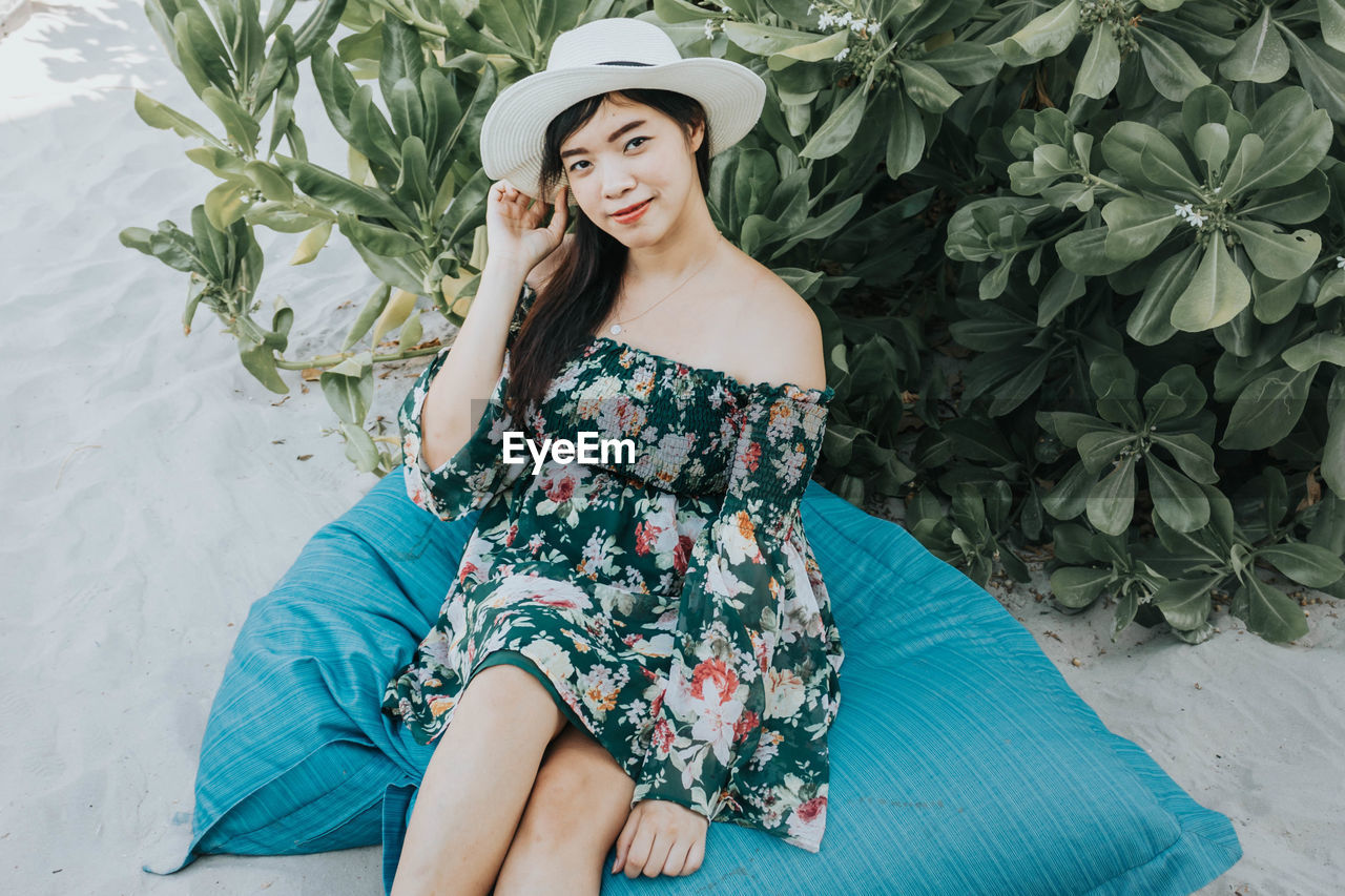 Portrait of smiling woman wearing hat sitting at beach