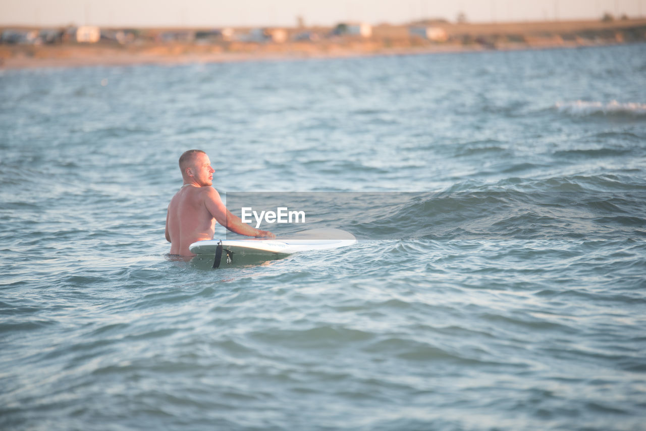 Rear view of shirtless male surfer with surfboard in sea