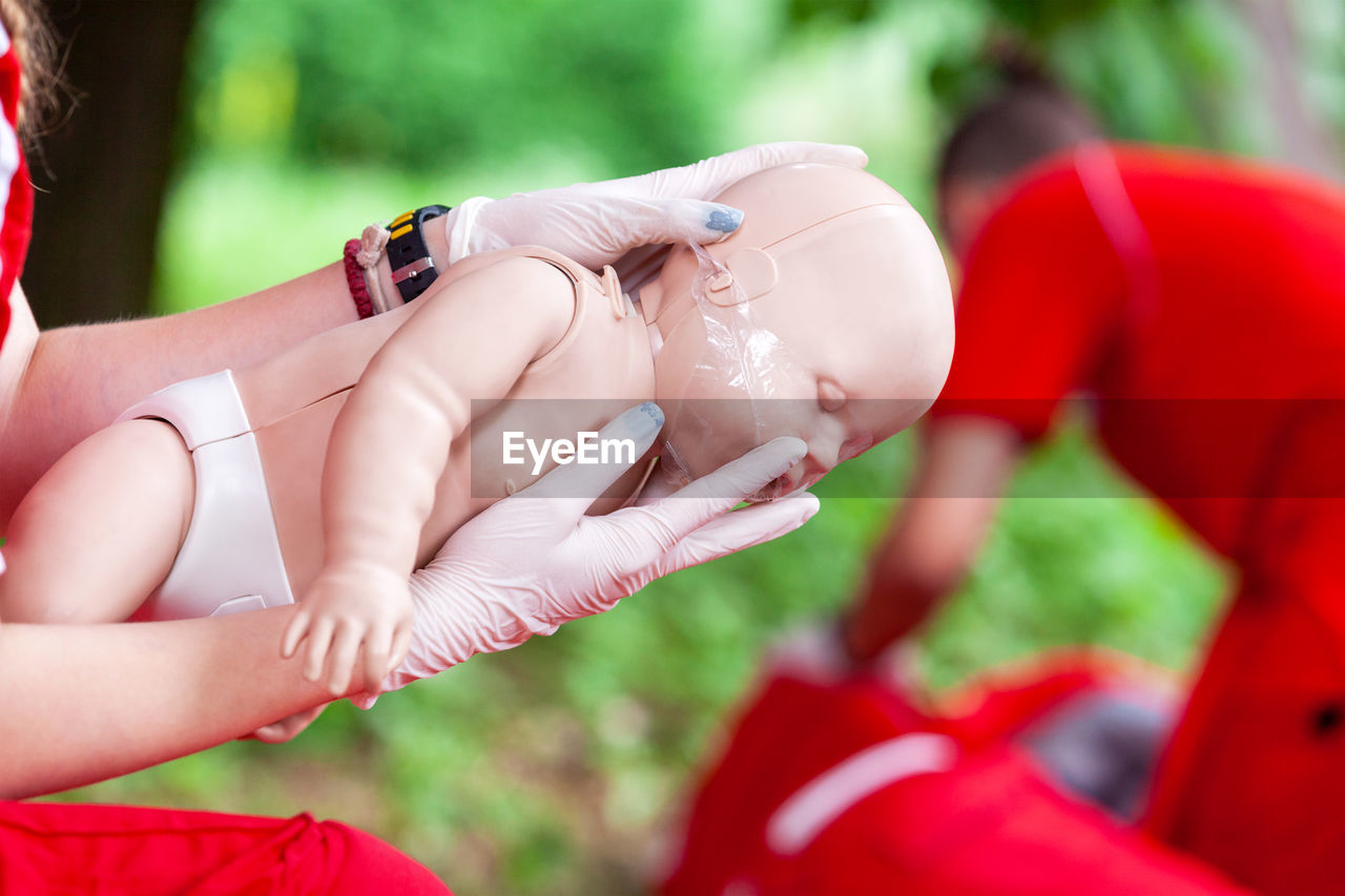 Close-up of female paramedic worker training on baby doll outdoors