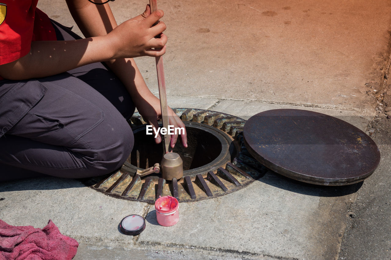 Midsection of person repairing manhole on sidewalk