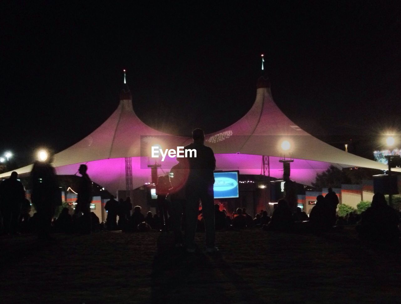 PEOPLE IN ILLUMINATED AMUSEMENT PARK AT NIGHT