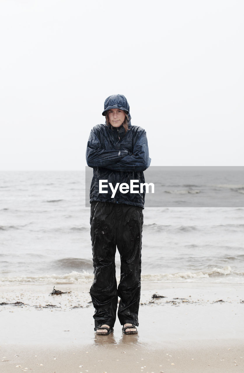 Portrait of woman wearing raincoat standing at sea shore during rainy season