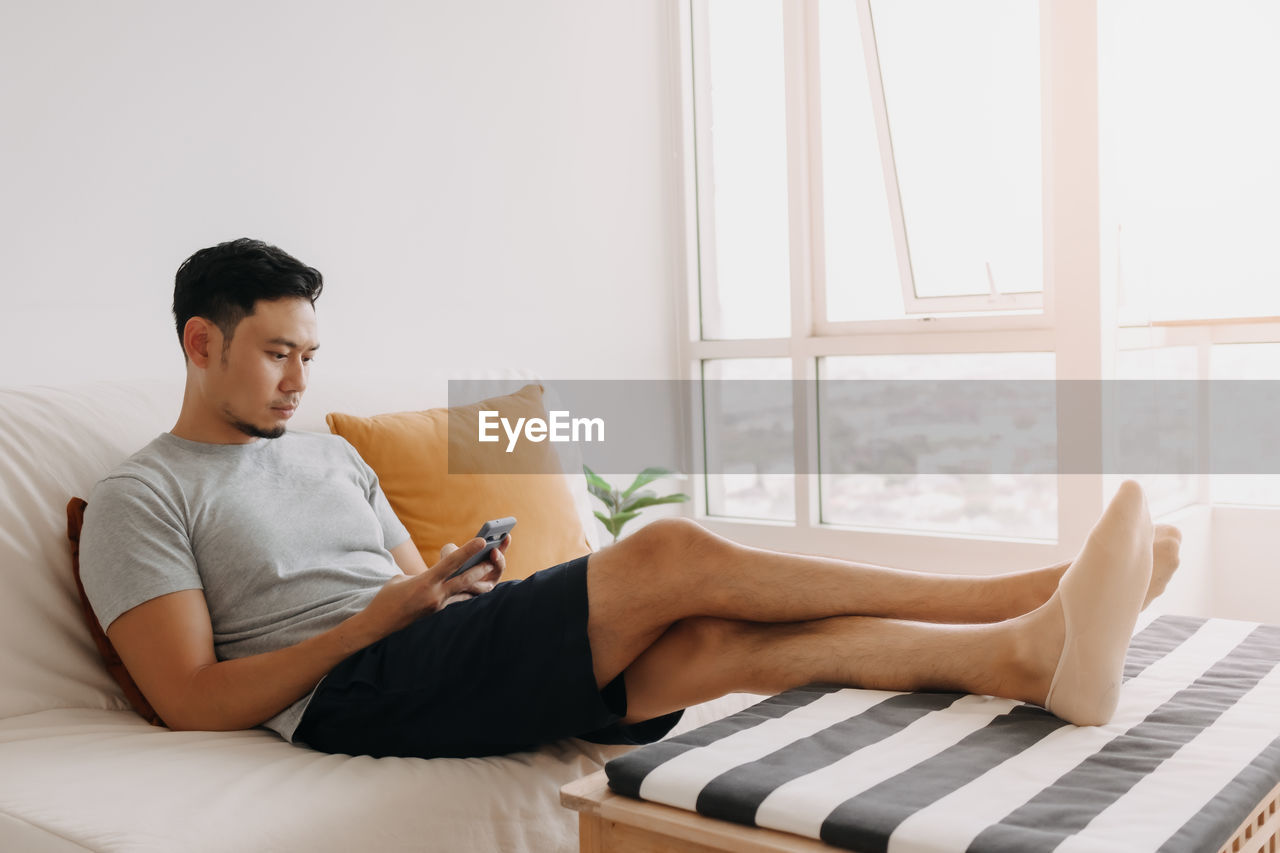 young woman using laptop while lying on bed at home