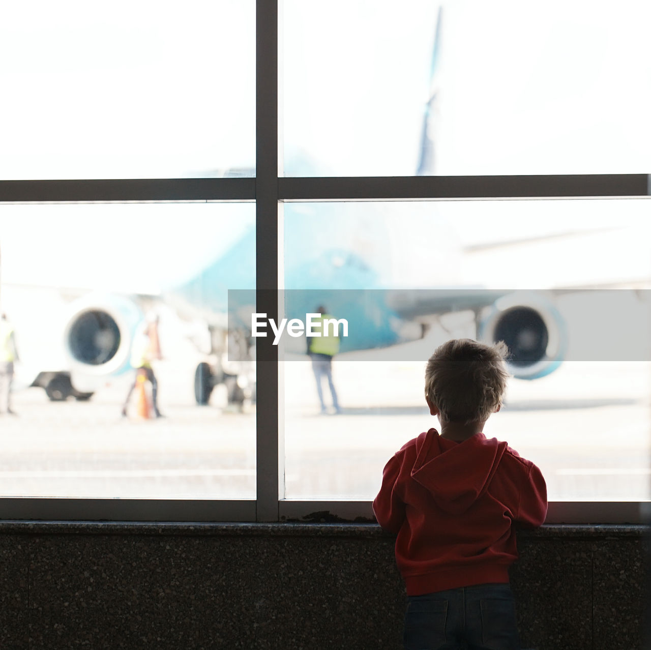 Rear view of boy looking through window at airport terminal