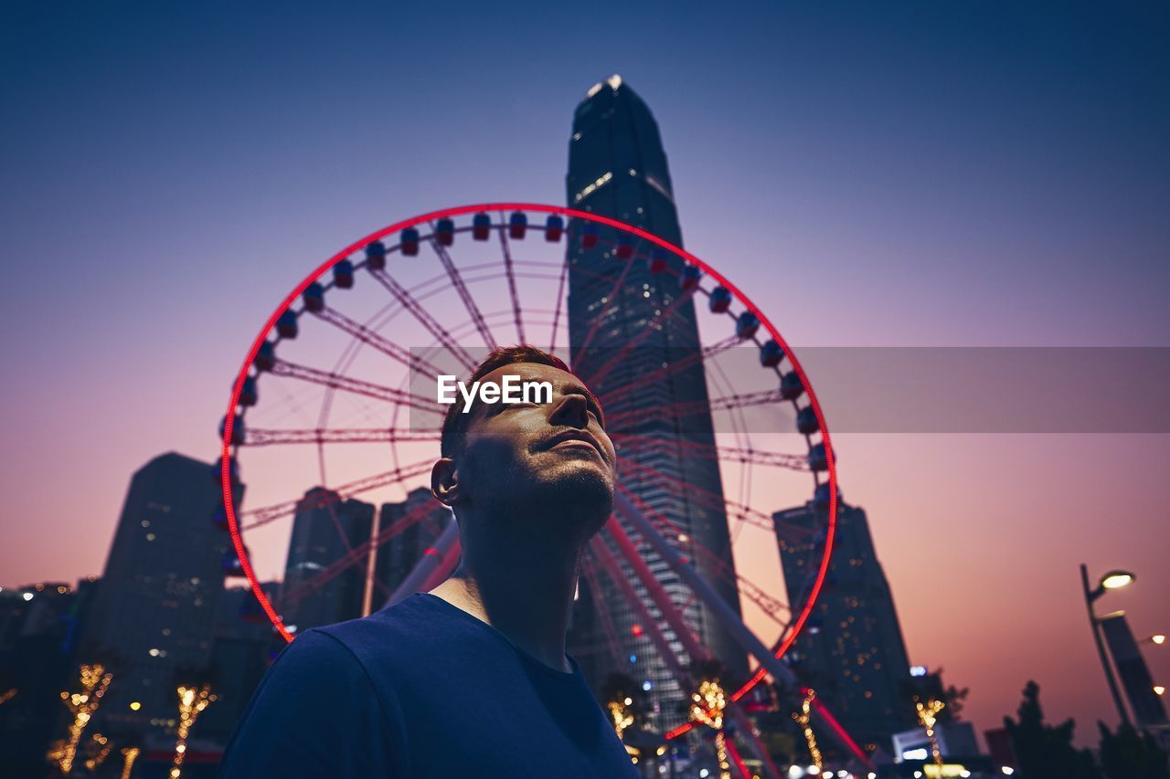 Low angle view of man against ferris wheel at dusk