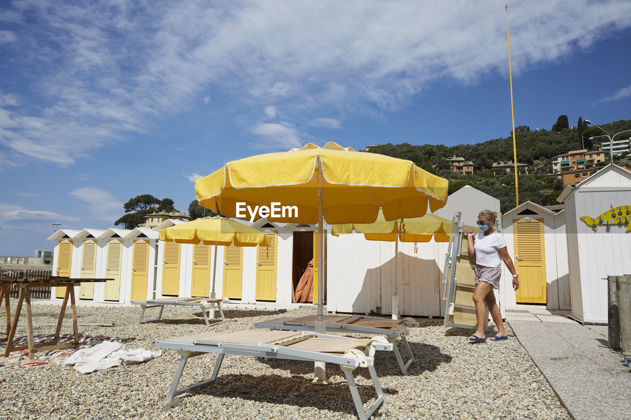 REAR VIEW OF MAN STANDING ON CHAIR AT BEACH