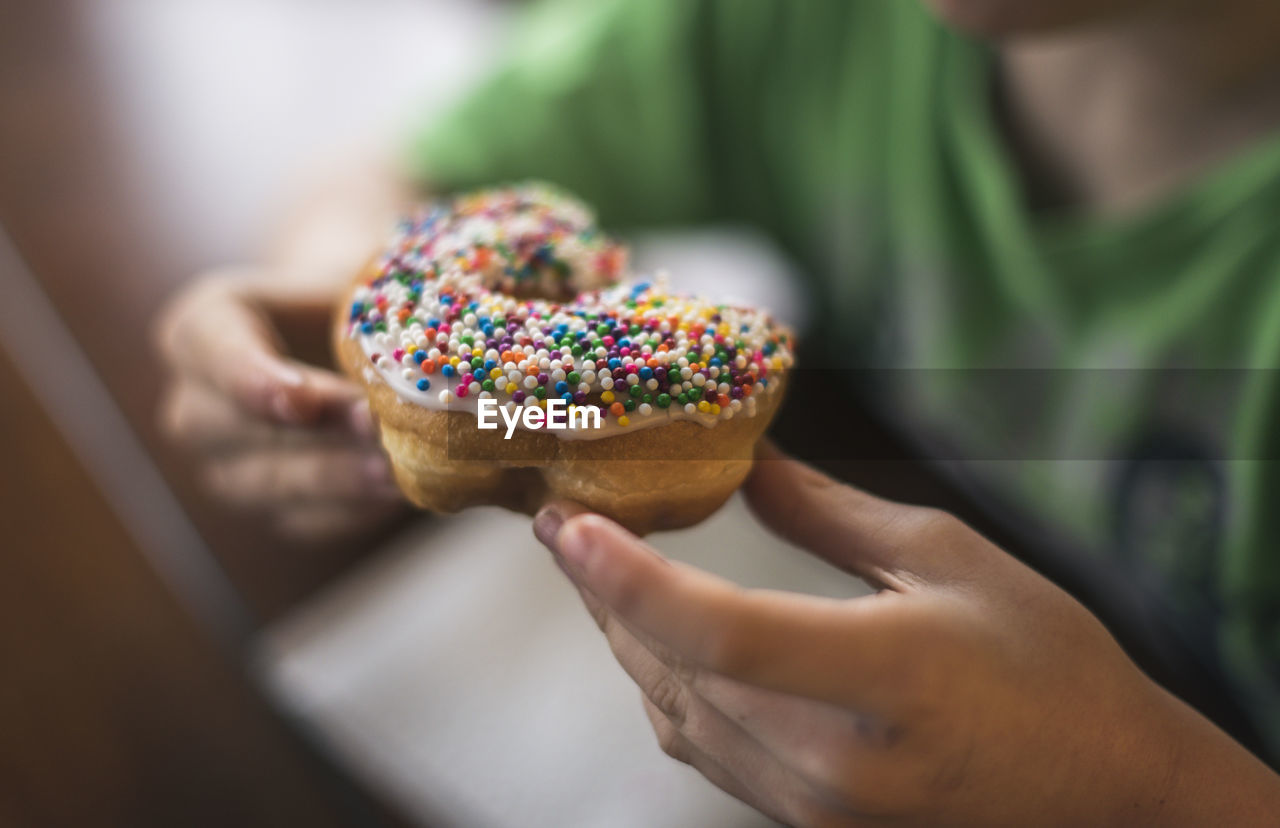 Midsection of boy eating donut while sitting by table at home