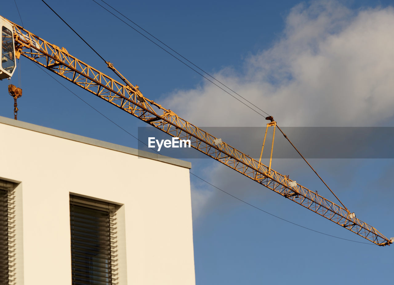 Crane boom in front of a bright blue sky above the corner of a new building, abstract