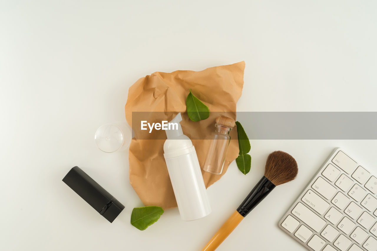 High angle view of laptop with beauty product and leaves on white background