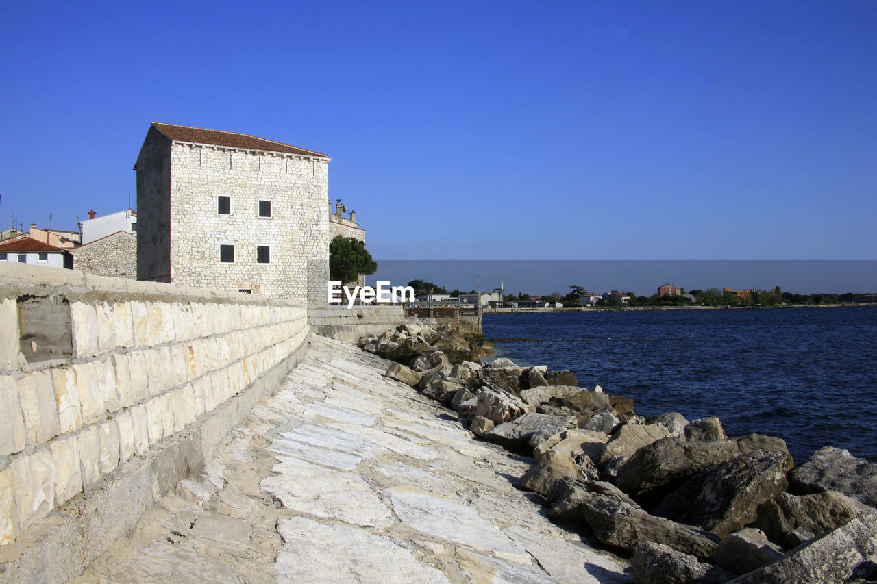 BUILDINGS BY SEA AGAINST BLUE SKY