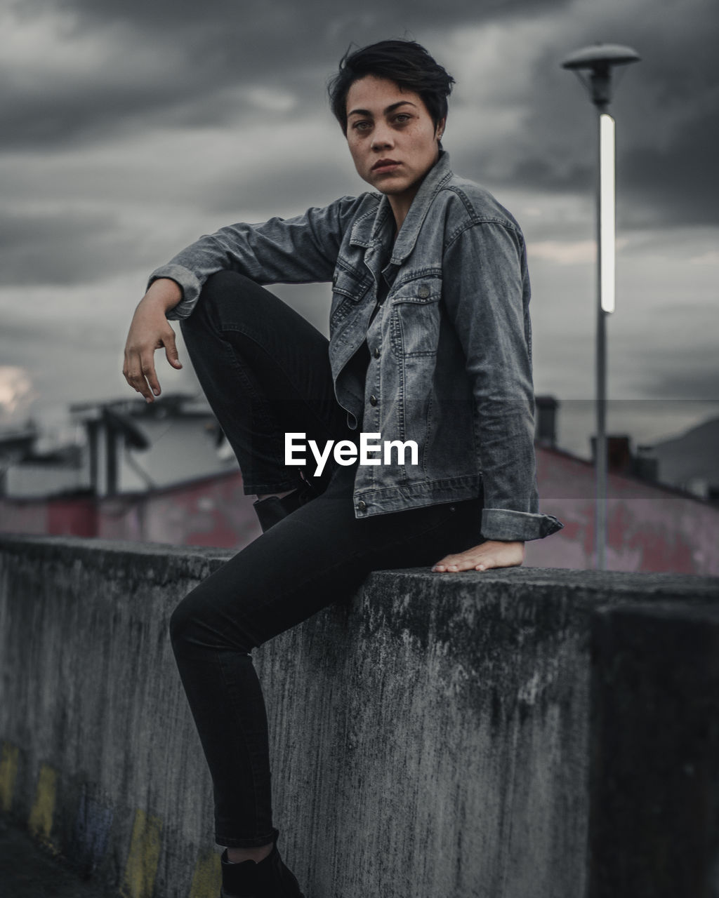 Portrait of woman sitting on retaining wall against sky