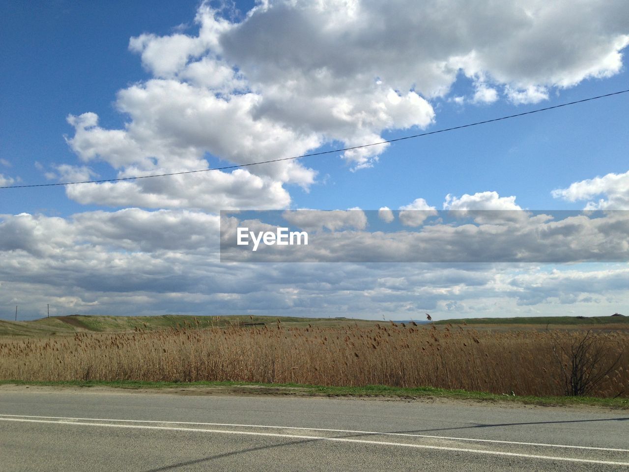 Road passing through field against cloudy sky