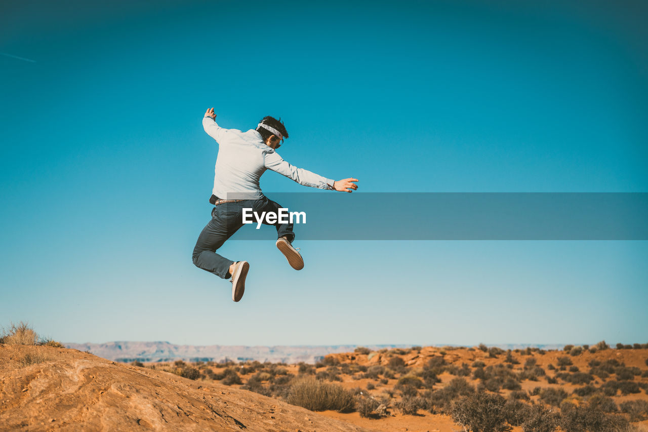 Low angle view of man jumping against clear sky