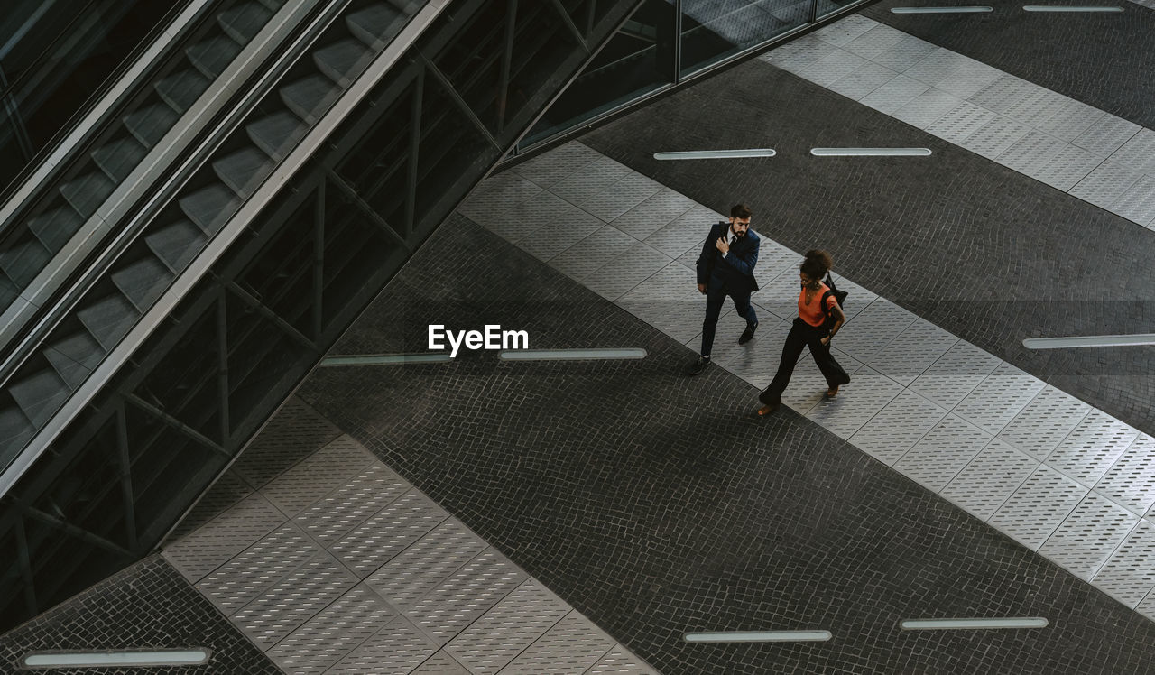 Male and female colleagues discussing while walking by escalator on walkway