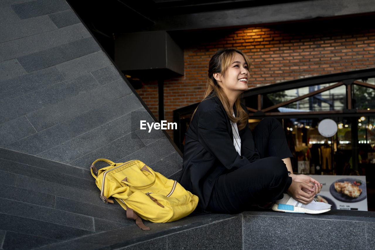 Smiling businesswoman with backpack sitting on retaining wall