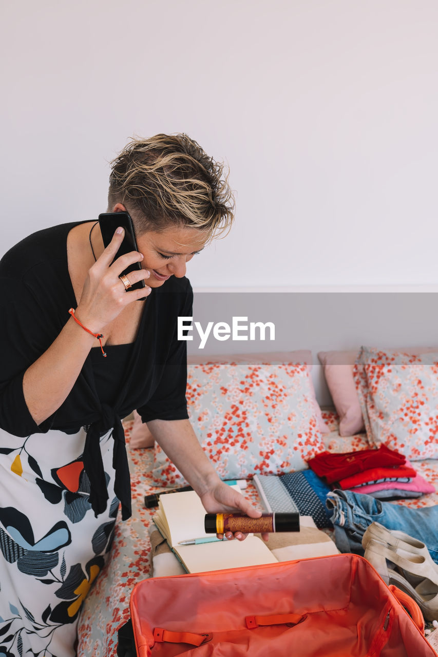 Side view of young woman using mobile phone while sitting on bed at home