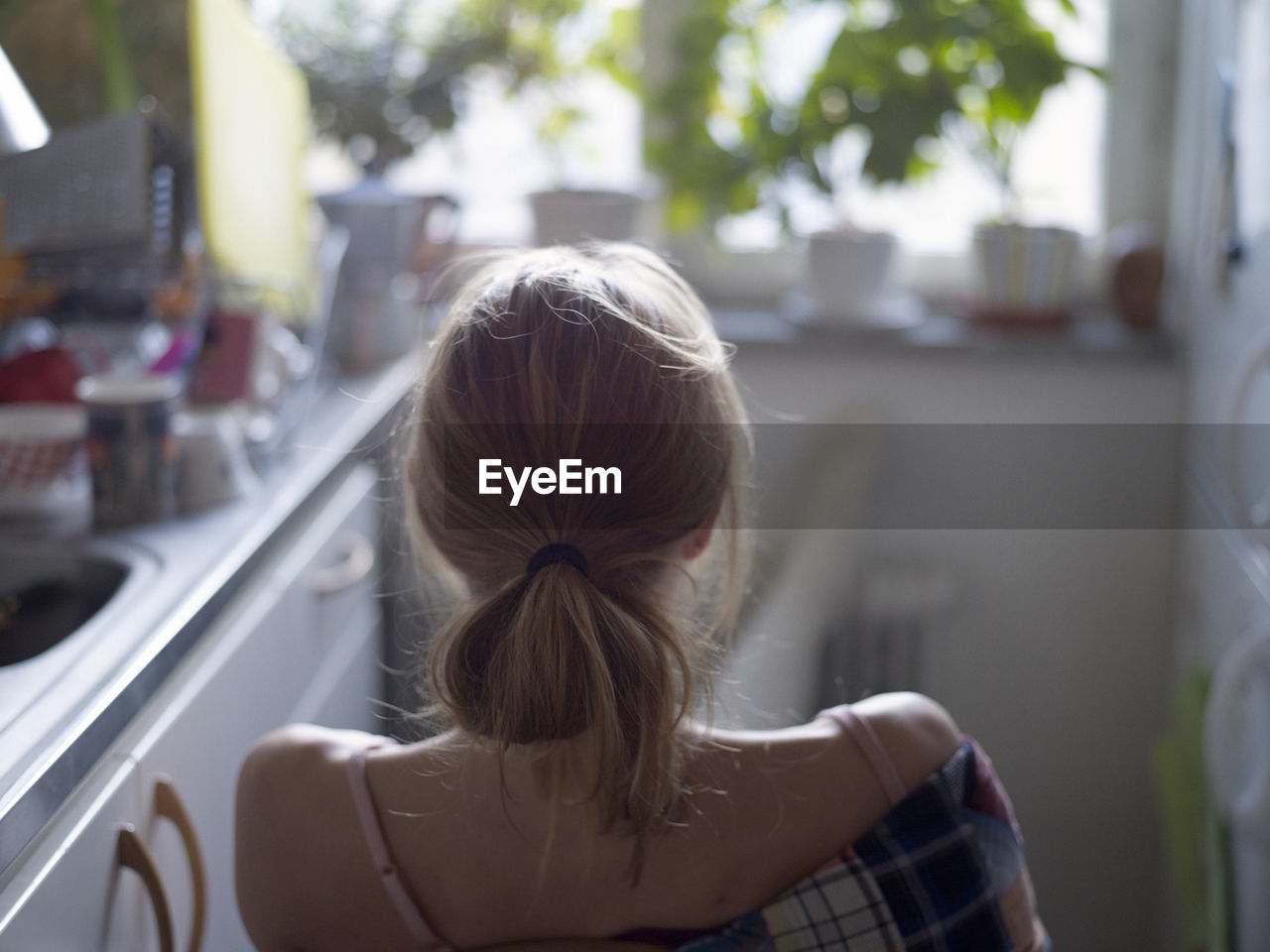 Young woman sitting in kitchen, rear view