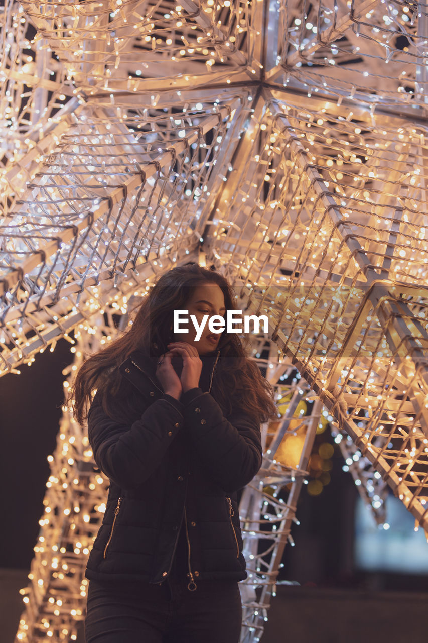 Woman wearing warm clothing against illuminated decoration at night