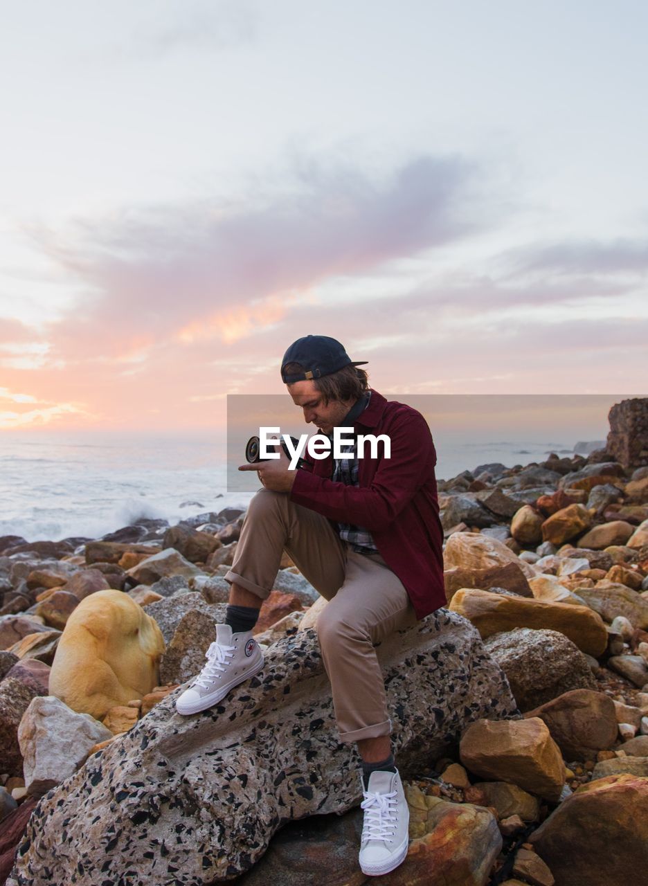 WOMAN PHOTOGRAPHING ON ROCK AT BEACH