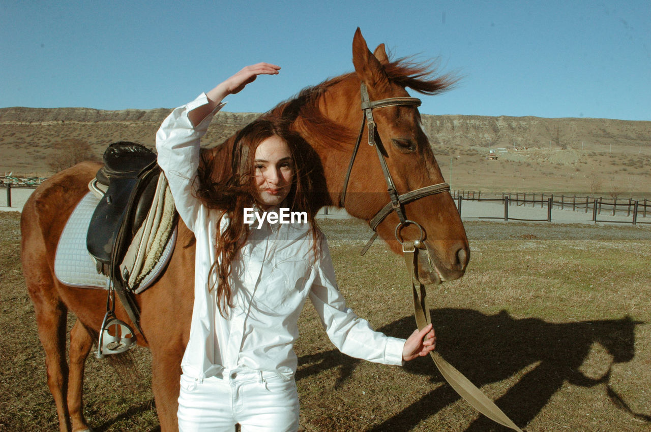 Portrait of young woman with horse standing on land against clear sky