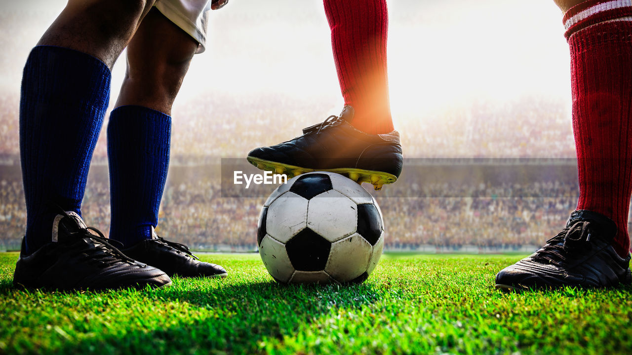 Low section of players standing soccer ball on field