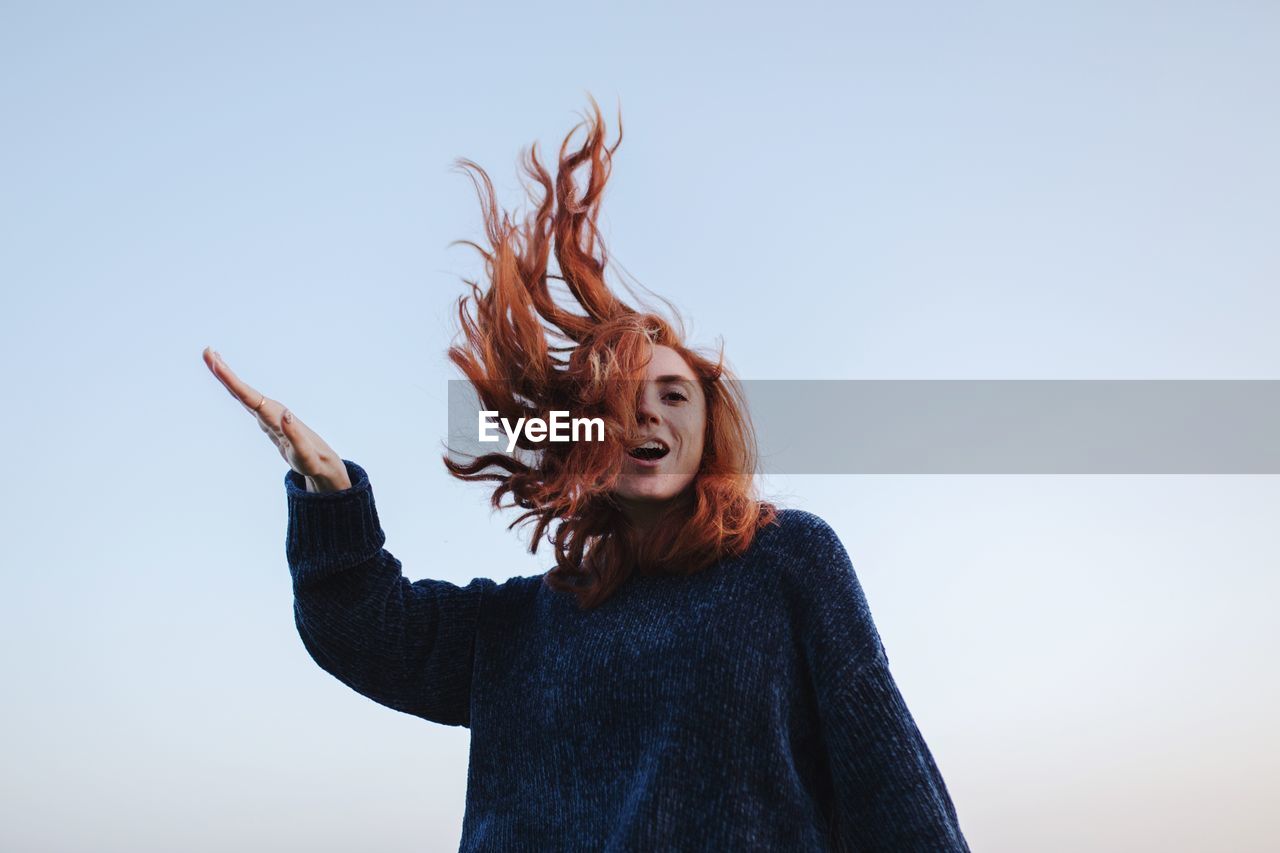 Low angle view of cheerful woman against clear sky