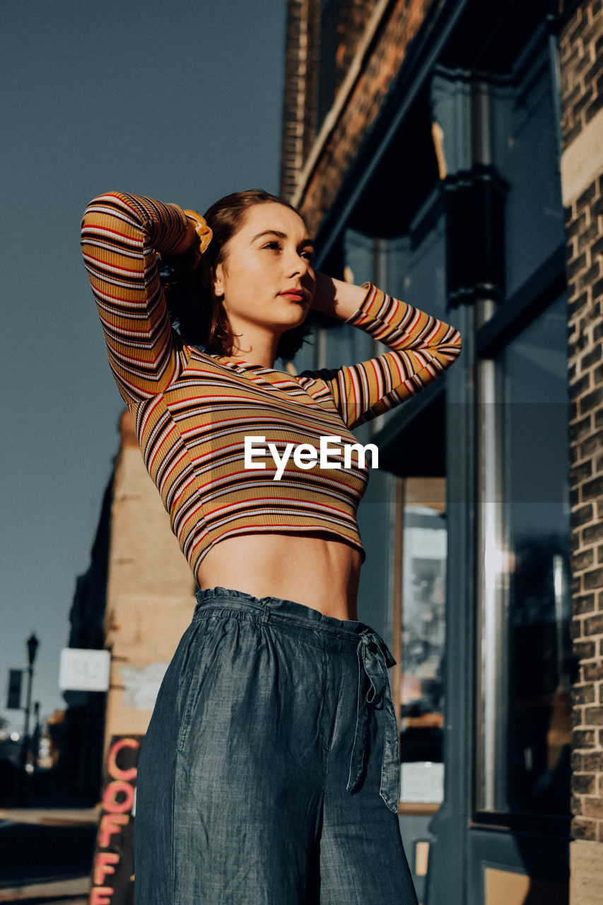 Young woman looking away while standing against buildings