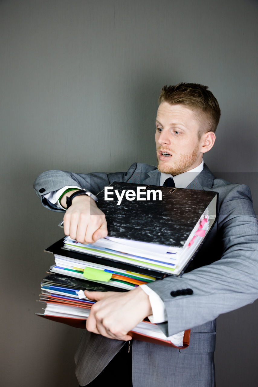 Tired businessman holding stacked files against gray background