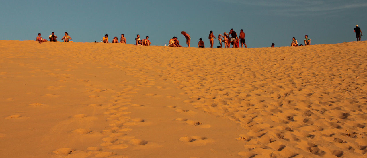 LOW ANGLE VIEW OF PEOPLE STANDING ON SAND AT BEACH