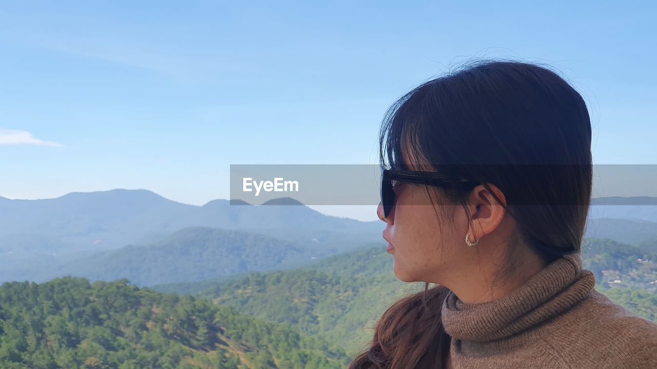 Portrait of woman looking at mountains against sky