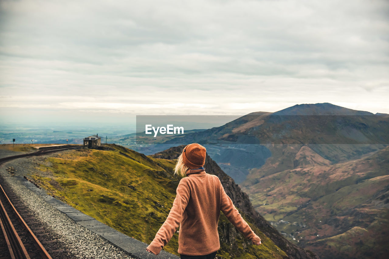 Rear view of woman looking at mountain against cloudy sky