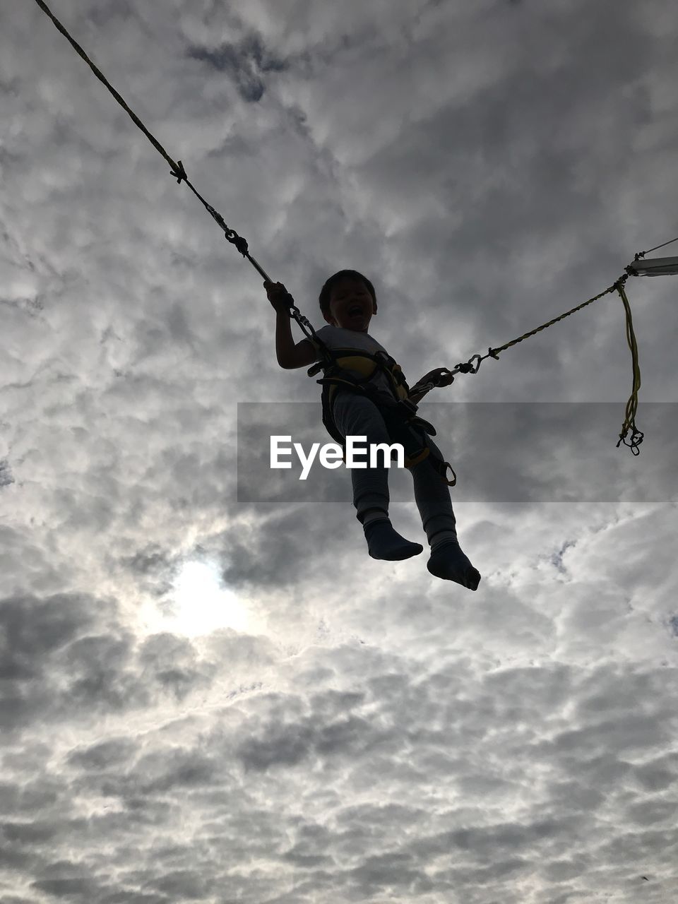 Low angle view of boy zip lining against cloudy sky