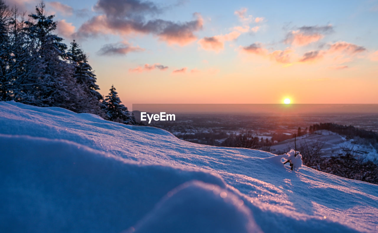 Snow covered landscape against sky during sunset