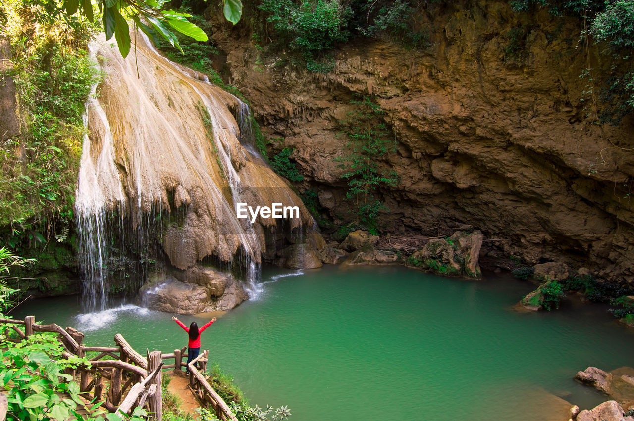 A woman is admiring the beauty of a green waterfall koh luang waterfall, lamphun