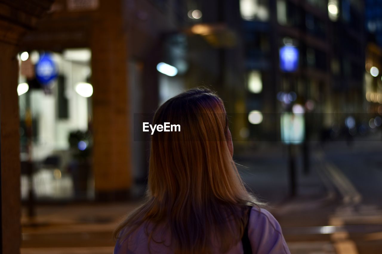 Rear view of woman standing against illuminated city at night