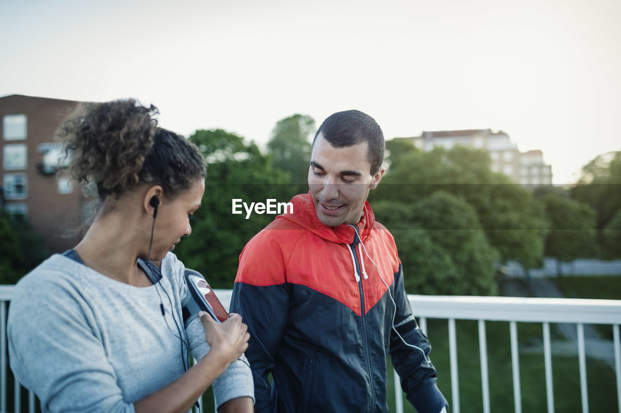 Man looking at woman using smart phone armband while walking at sidewalk