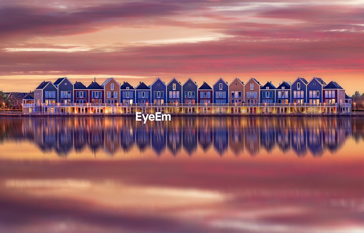 Reflection of illuminated houses on lake against cloudy sky