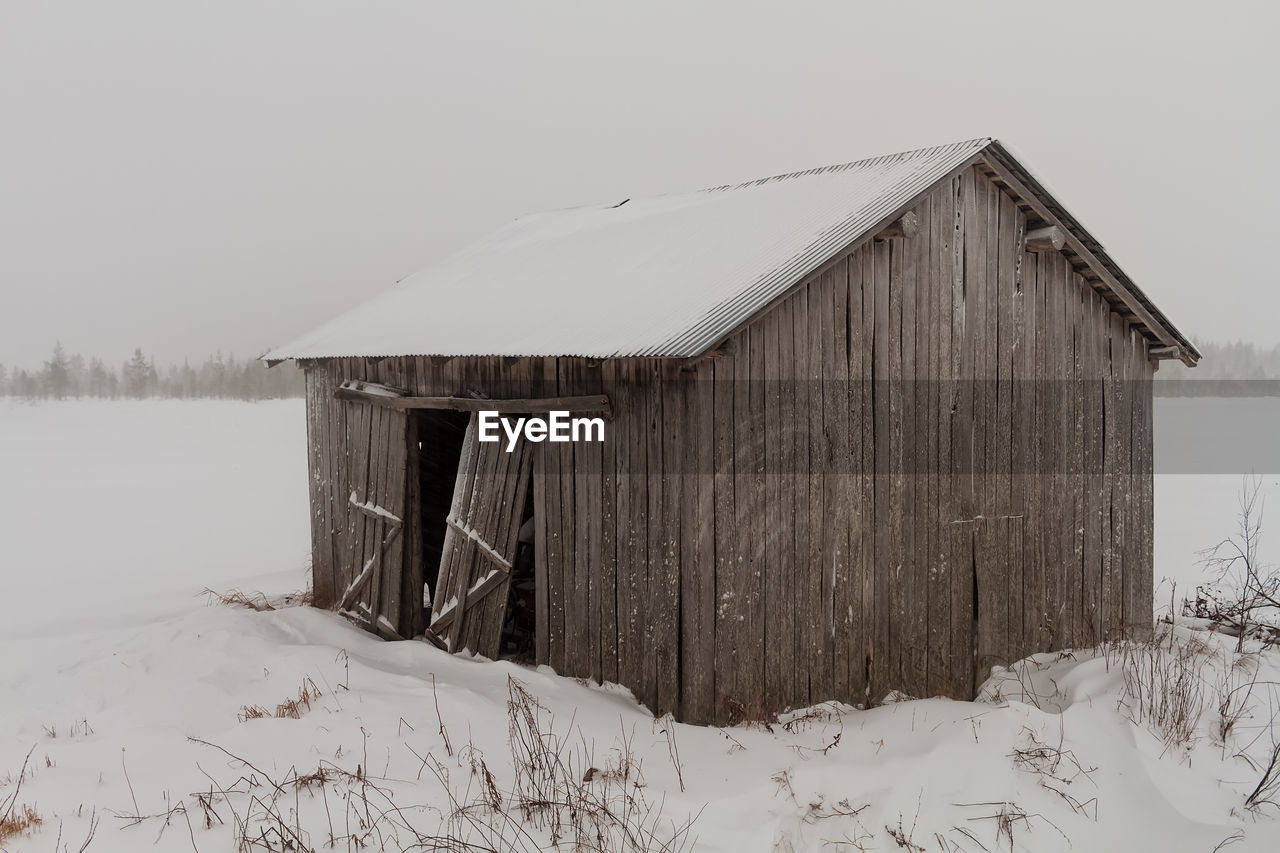 HOUSE ON SNOW COVERED FIELD BY HOUSES AGAINST SKY