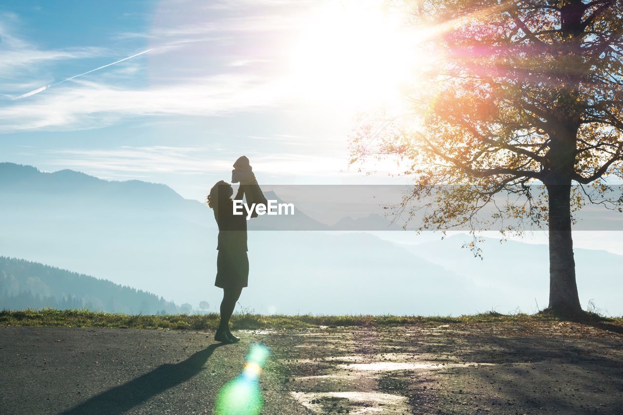 Woman with baby standing on road against sky during sunset