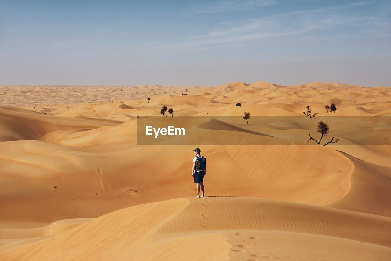 Rear view of man standing on sand dune in desert against sky