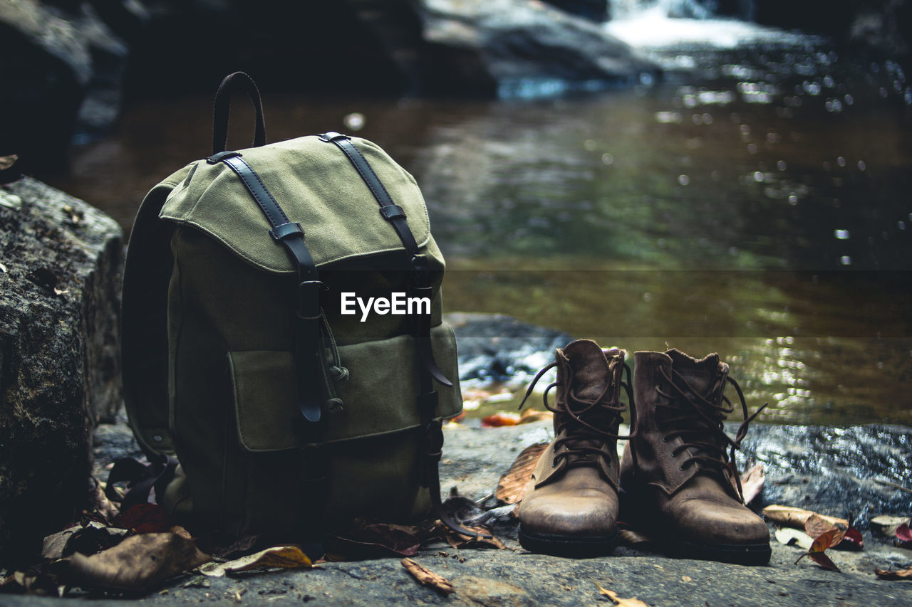Close-up of backpack and boots on rock against river