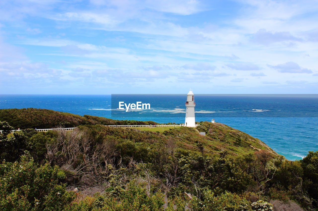 LIGHTHOUSE AMIDST SEA AND PLANTS AGAINST SKY