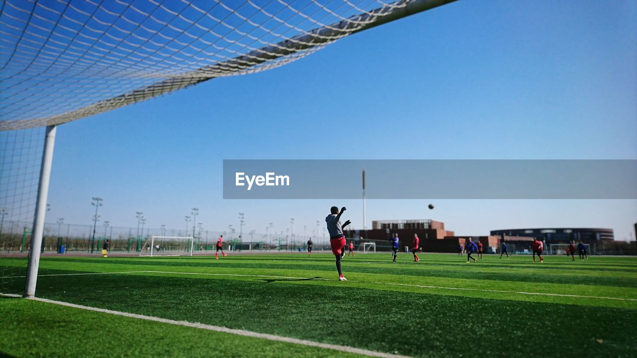 Players playing soccer on field against clear sky