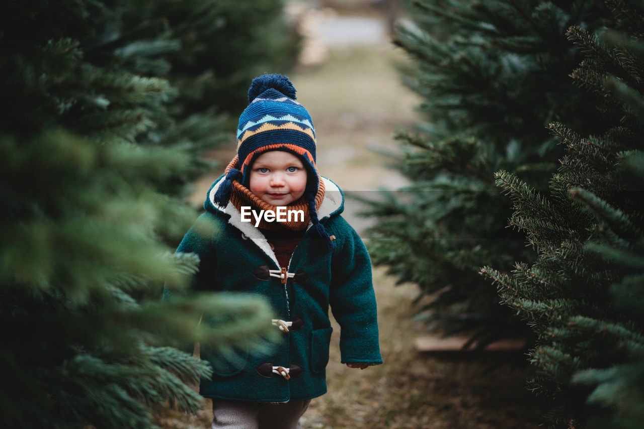 Adorable child wearing wool coat walking between christmas trees