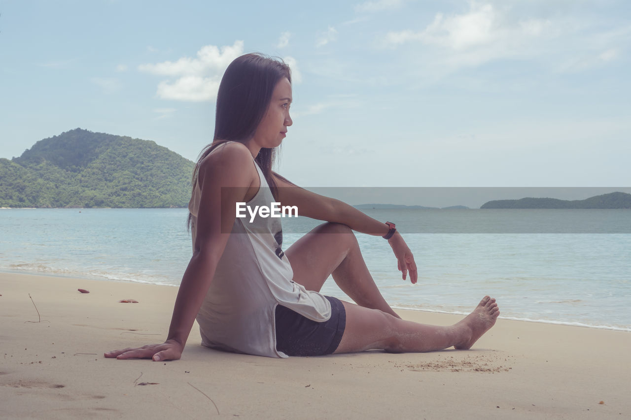 Young woman sitting on beach against sky