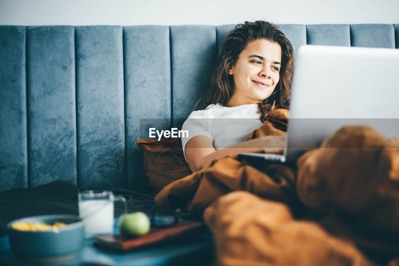 portrait of woman using mobile phone while sitting on sofa at home