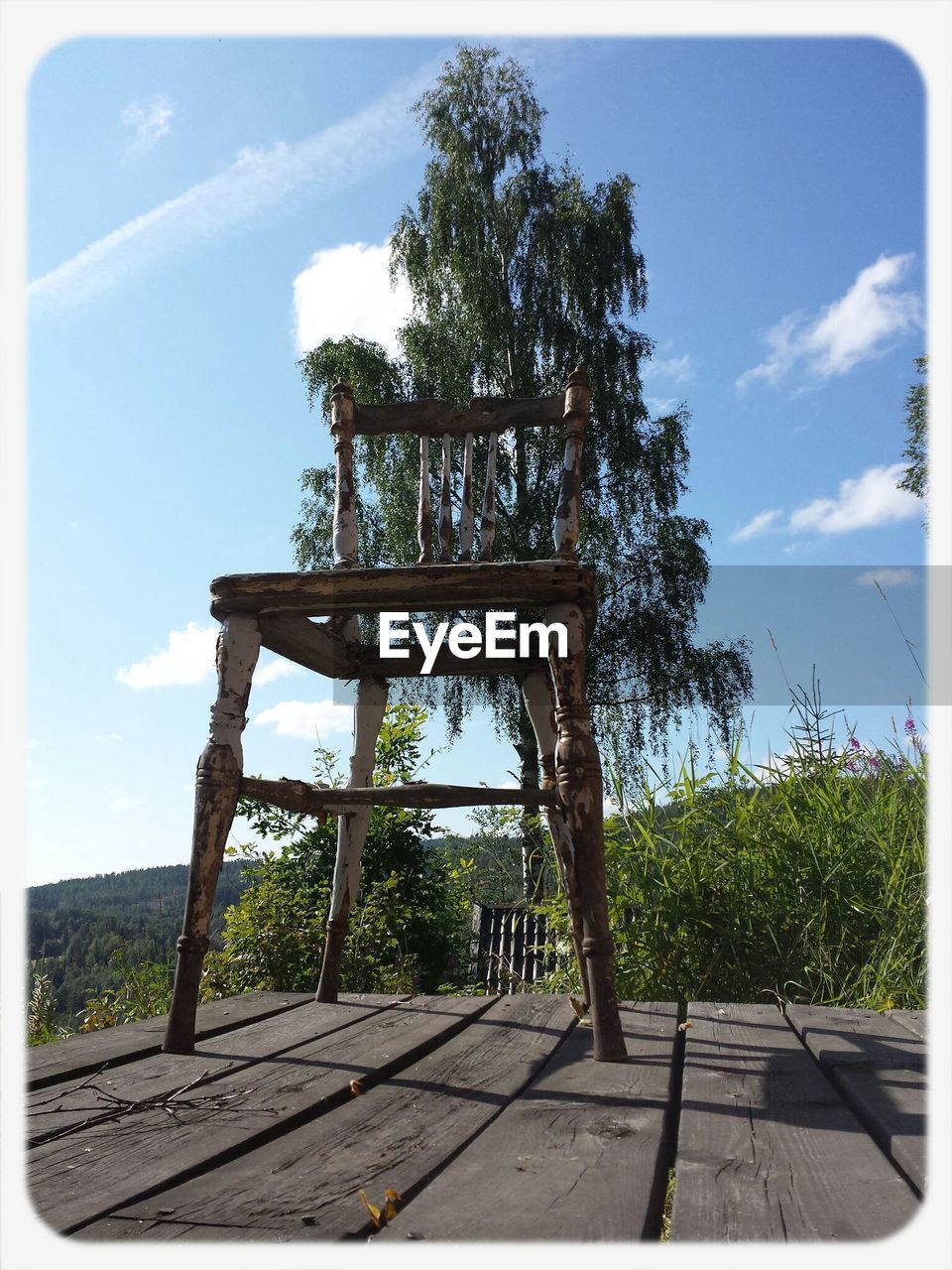 Low angle view of empty chair against tree and blue sky